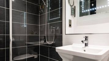 Une salle de bain moderne avec une douche à parois de verre, un lavabo blanc et un miroir avec éclairage intégré.