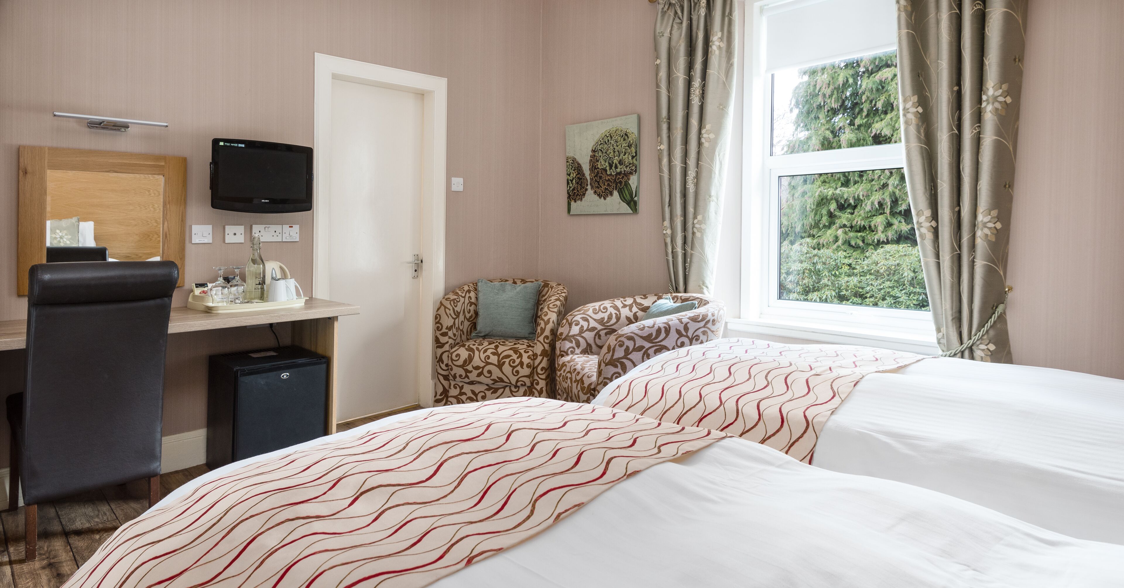 A hotel room with a bed, a desk with a computer, a chair, and a window with curtains.
