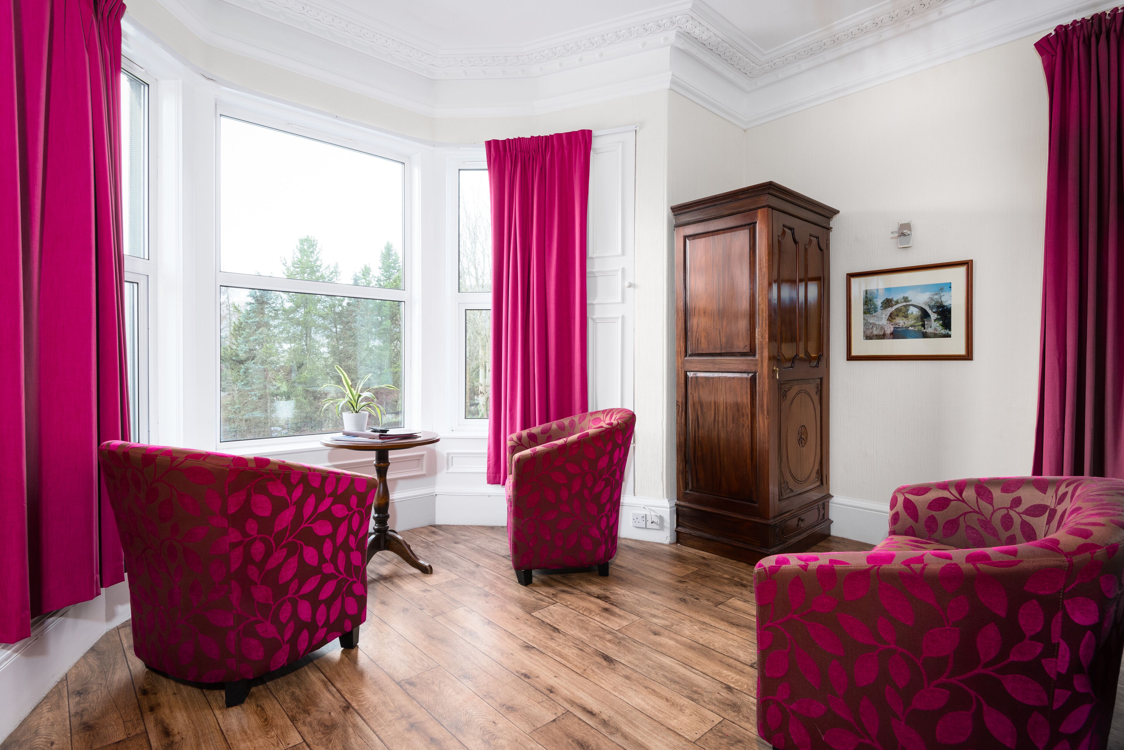 A room with two patterned armchairs, a wooden cabinet, and a window with curtains.