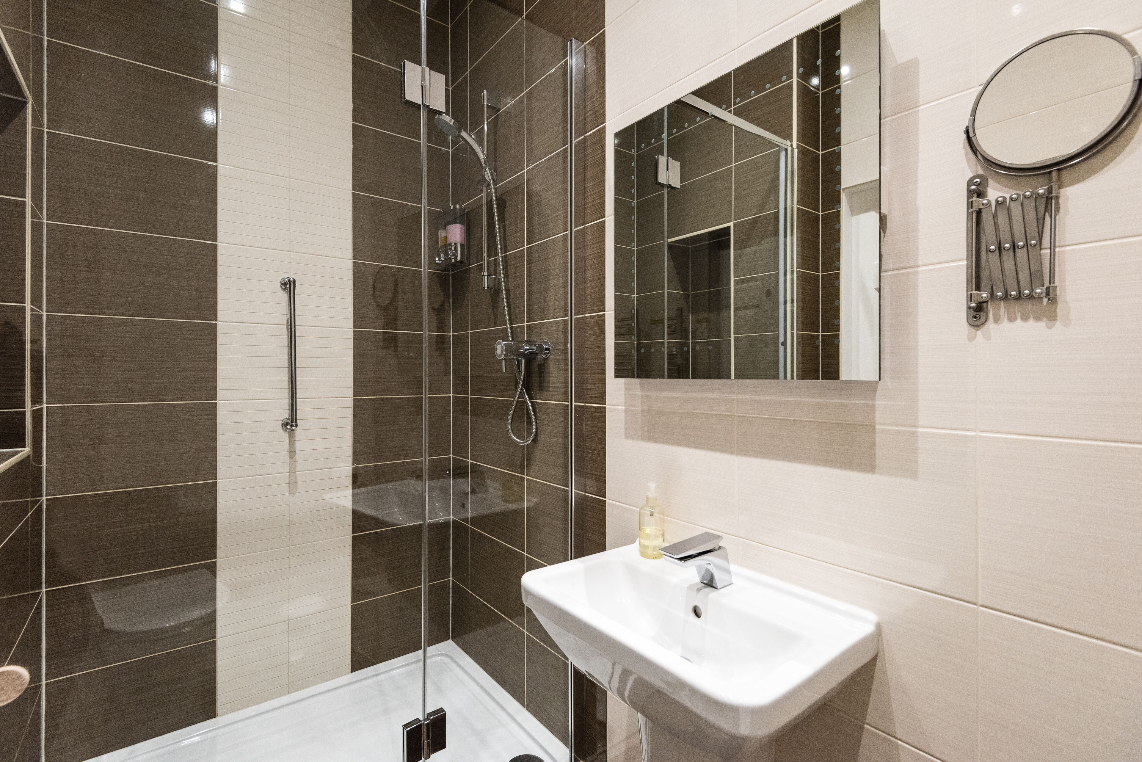 Une salle de bain moderne avec une douche à parois de verre, un lavabo blanc et un miroir doté d’un porte-serviettes.