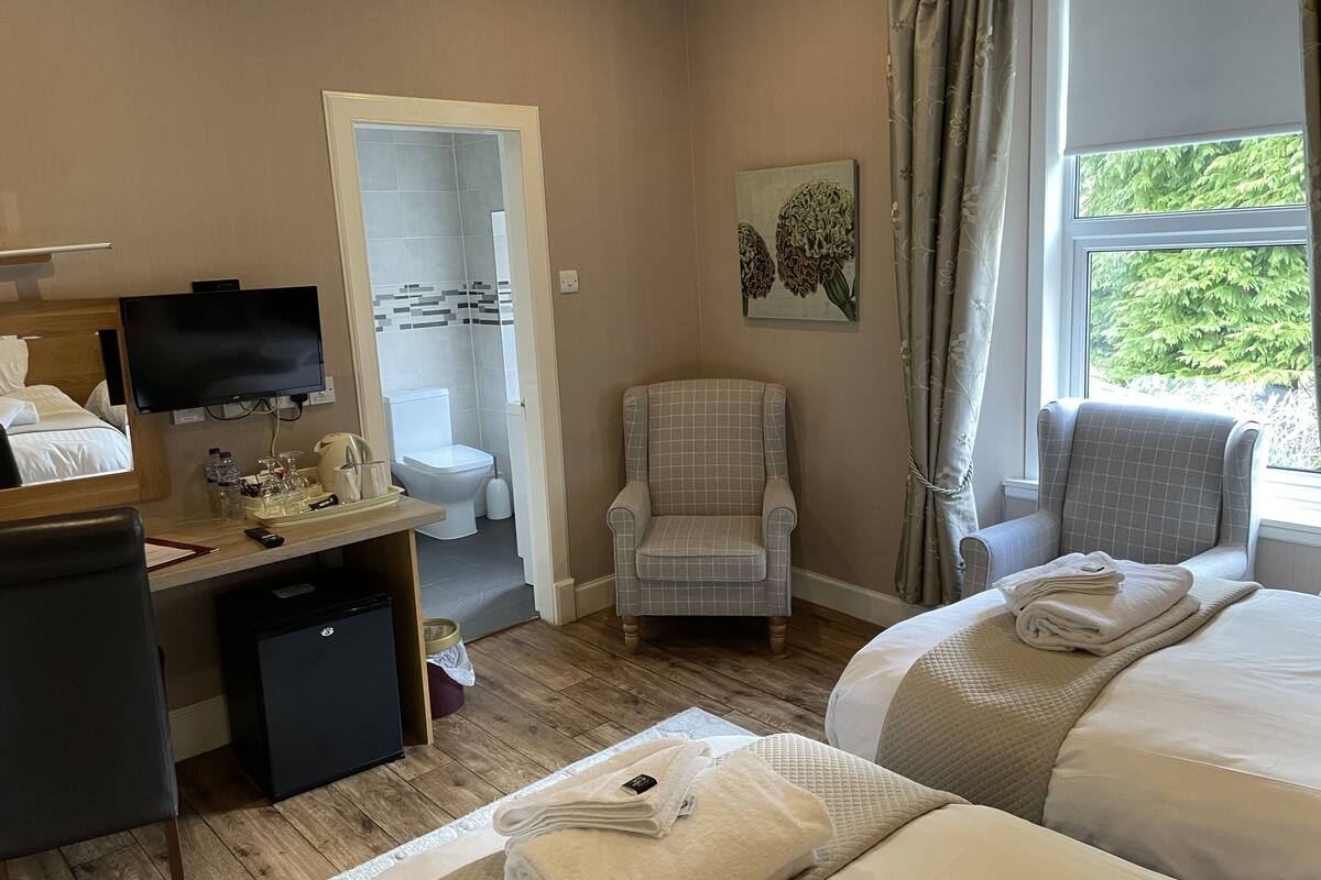 Habitación de hotel con cama, escritorio con televisor, una silla y vistas a zonas verdes por la ventana.