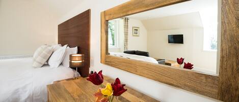 A bedroom with a bed, bedside lamp, wooden nightstand, and a mirror reflecting the room.