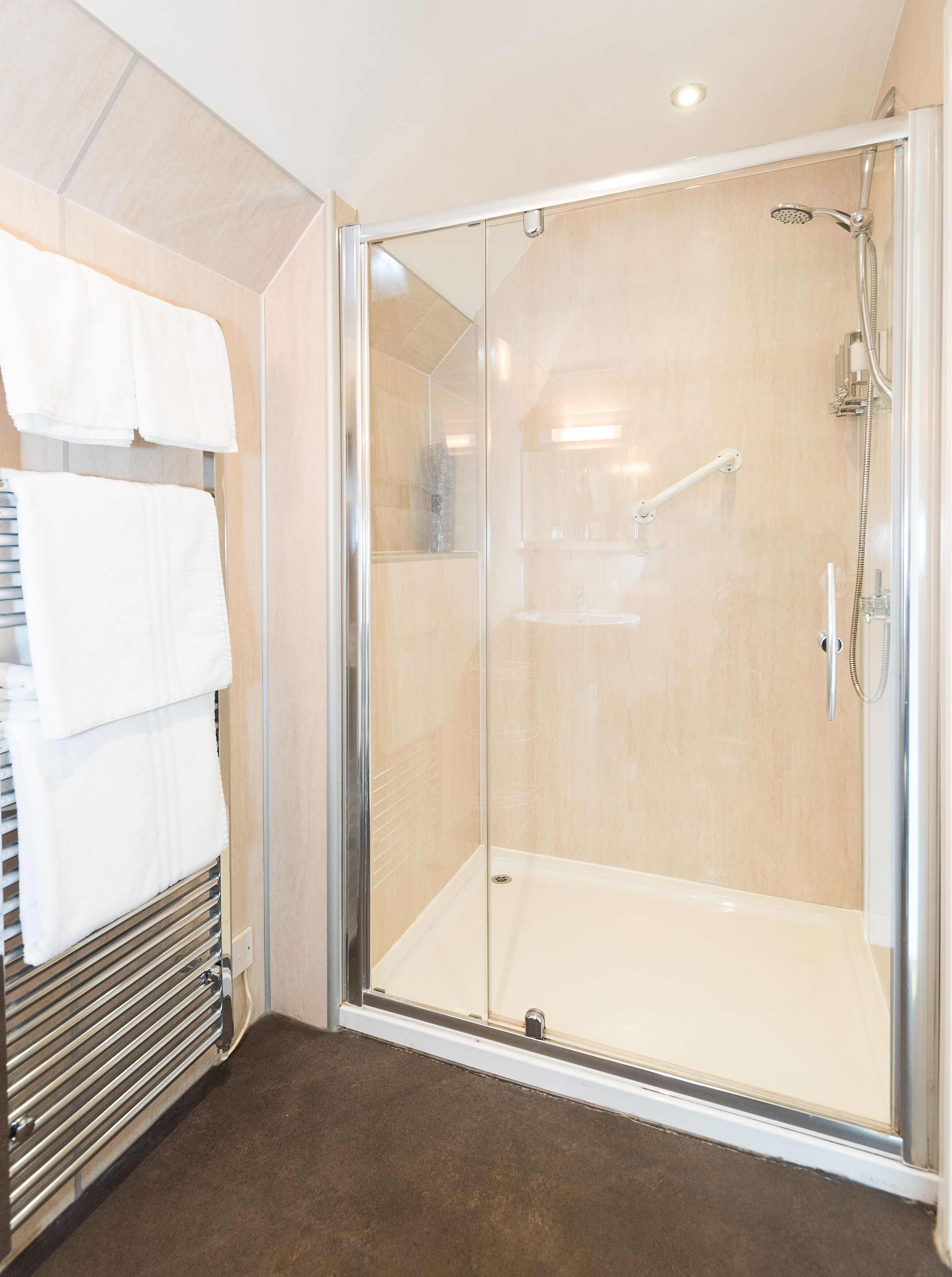 A modern bathroom with a glass-enclosed shower, a towel rack with white towels, and a beige tiled wall.