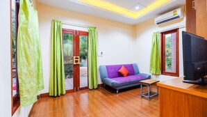 A living room with a sofa, a small table, and a TV. There are curtains on the windows and an air conditioning unit on the wall. - OYO 690 Bann Supansa Resort (Krabi)
