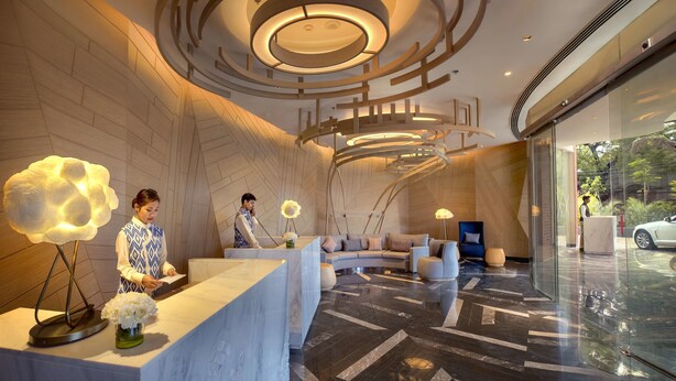 A modern hotel lobby with a reception desk, seating area, and a large glass entrance.