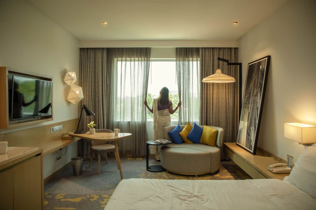 Een hotelkamer met een bed, een bureau, een stoel, een televisie, een raam met gordijnen en een schilderij aan de muur.
