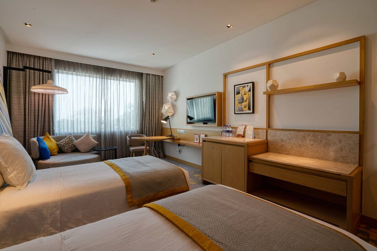 Hotelkamer met twee bedden, een bureau, een stoel, een televisie en een plank met decoratieve objecten.