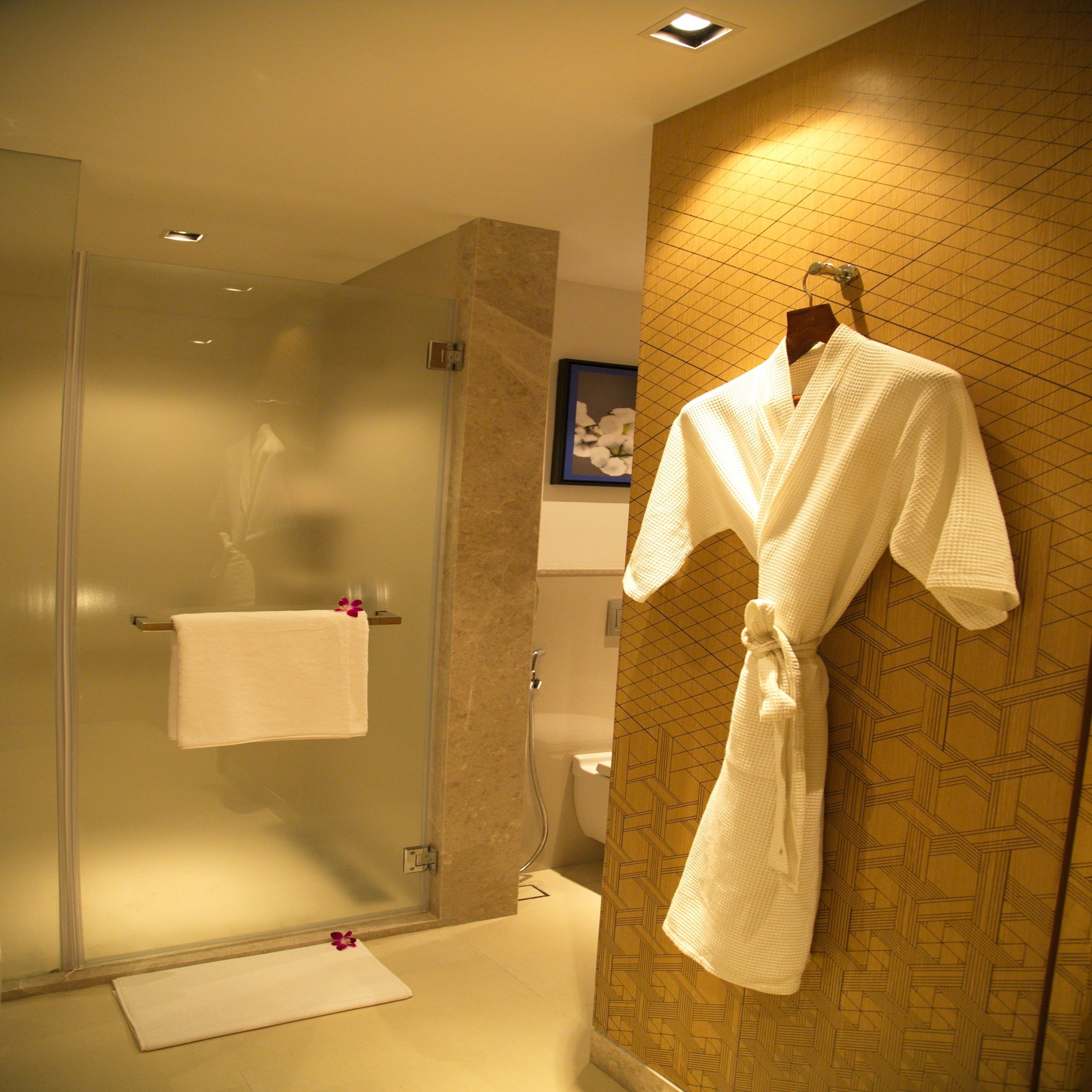 A bathroom with a glass shower enclosure, a white bathrobe hanging on the wall, and a white towel on a rack.