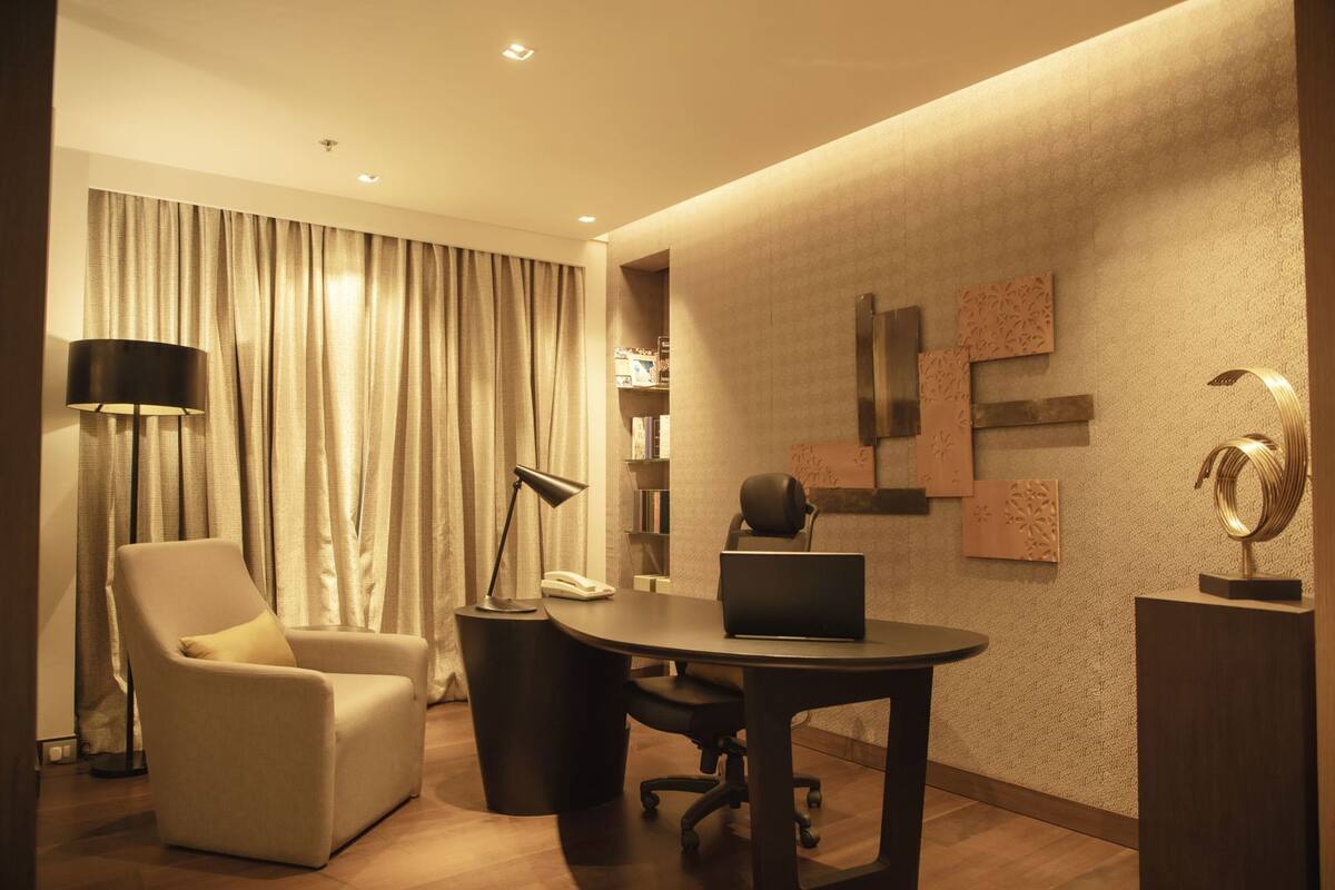 Een moderne hotelkamer met een ronde tafel, een stoel, een bureau, een lamp, een boekenplank en decoratieve wandkunst.
