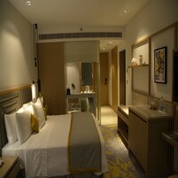 Una habitación de hotel con cama, mesita de noche, espejo y un escritorio pequeño con una silla.