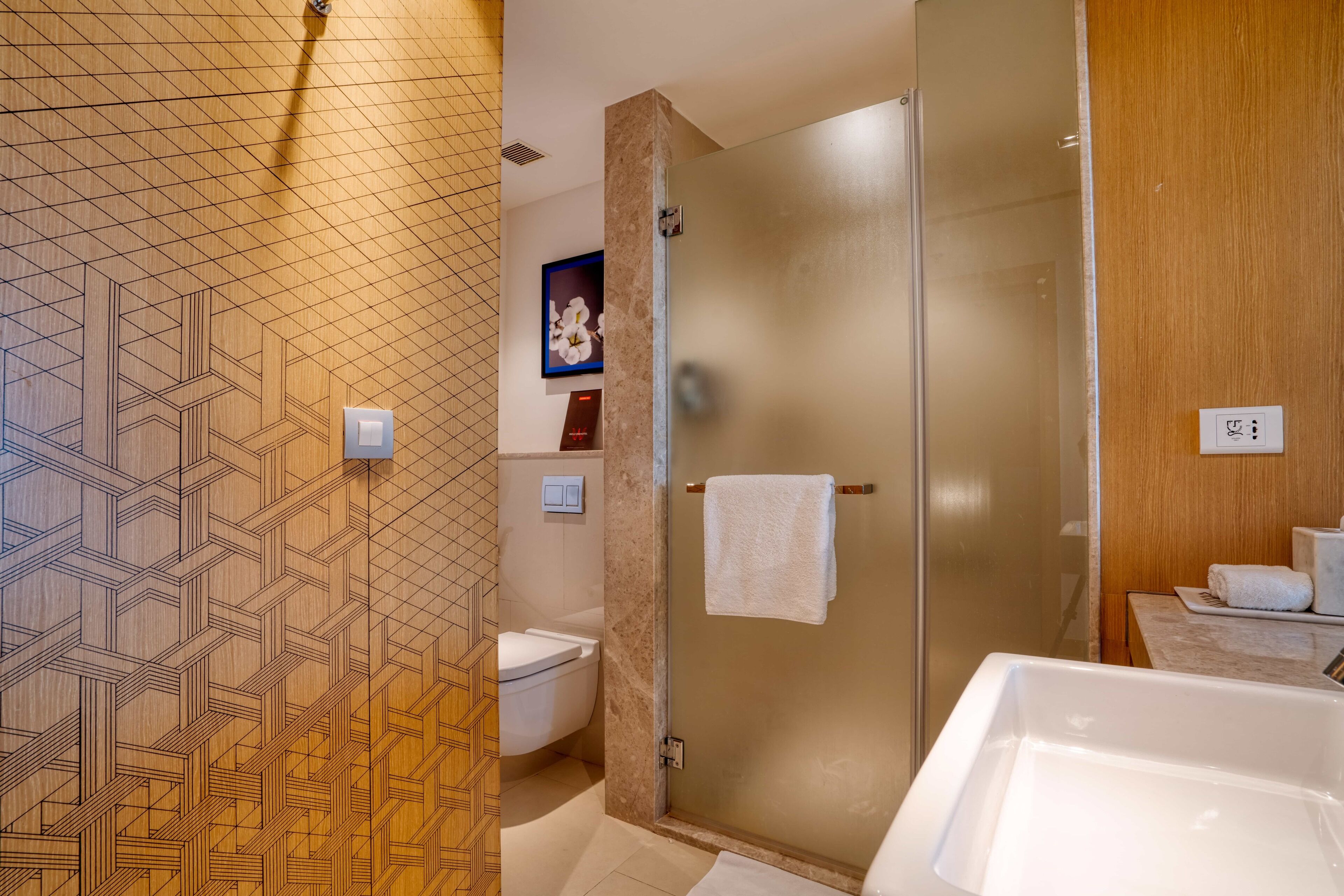 Une salle de bain moderne avec un mur orné d’un motif géométrique, une douche à parois de verre et une baignoire blanche.