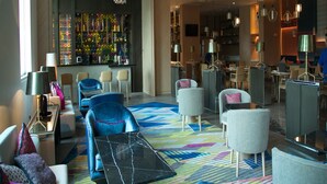 A modern hotel lobby with seating areas, a bar, and a dining space.
