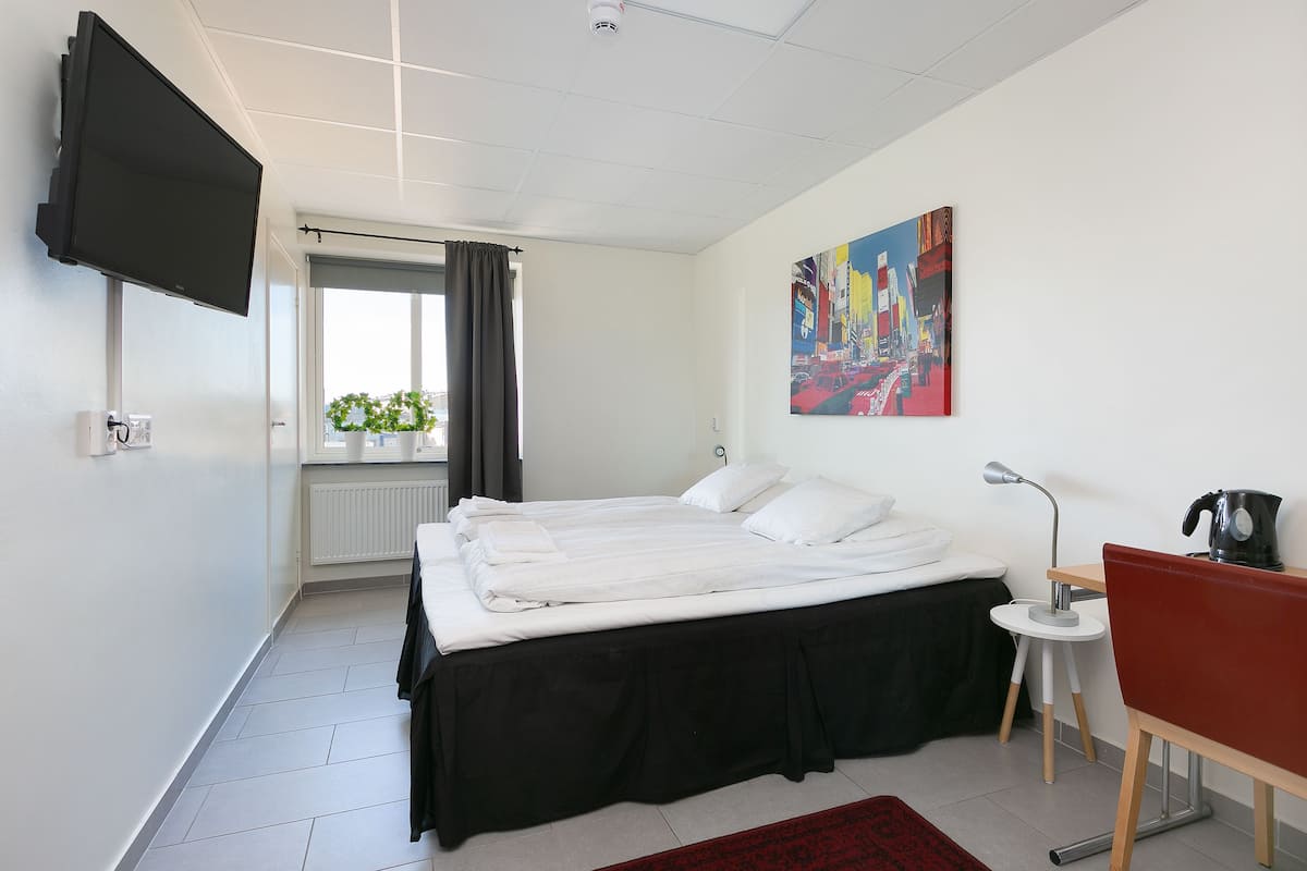 Una habitación de hotel moderna con una cama grande, un escritorio, una silla, un televisor y un cuadro en la pared.
