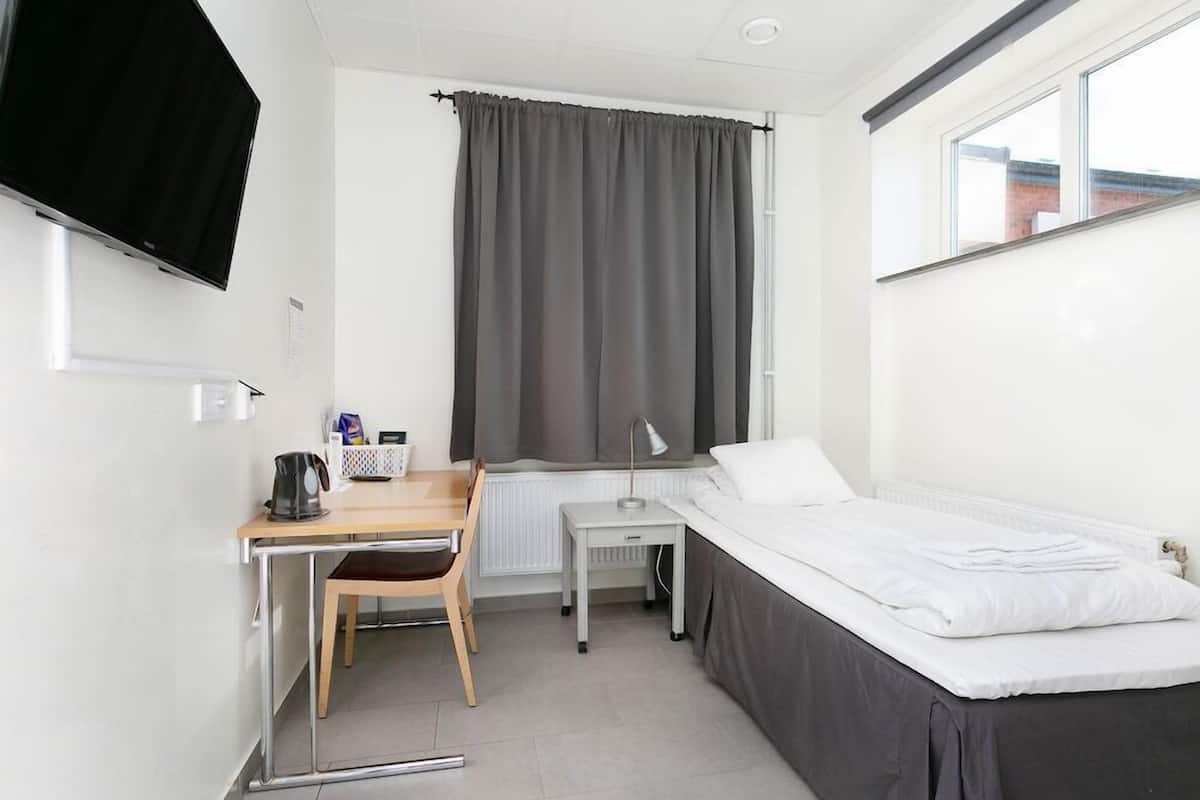 Una habitación con cama, escritorio, silla, televisor y ventana con cortinas.