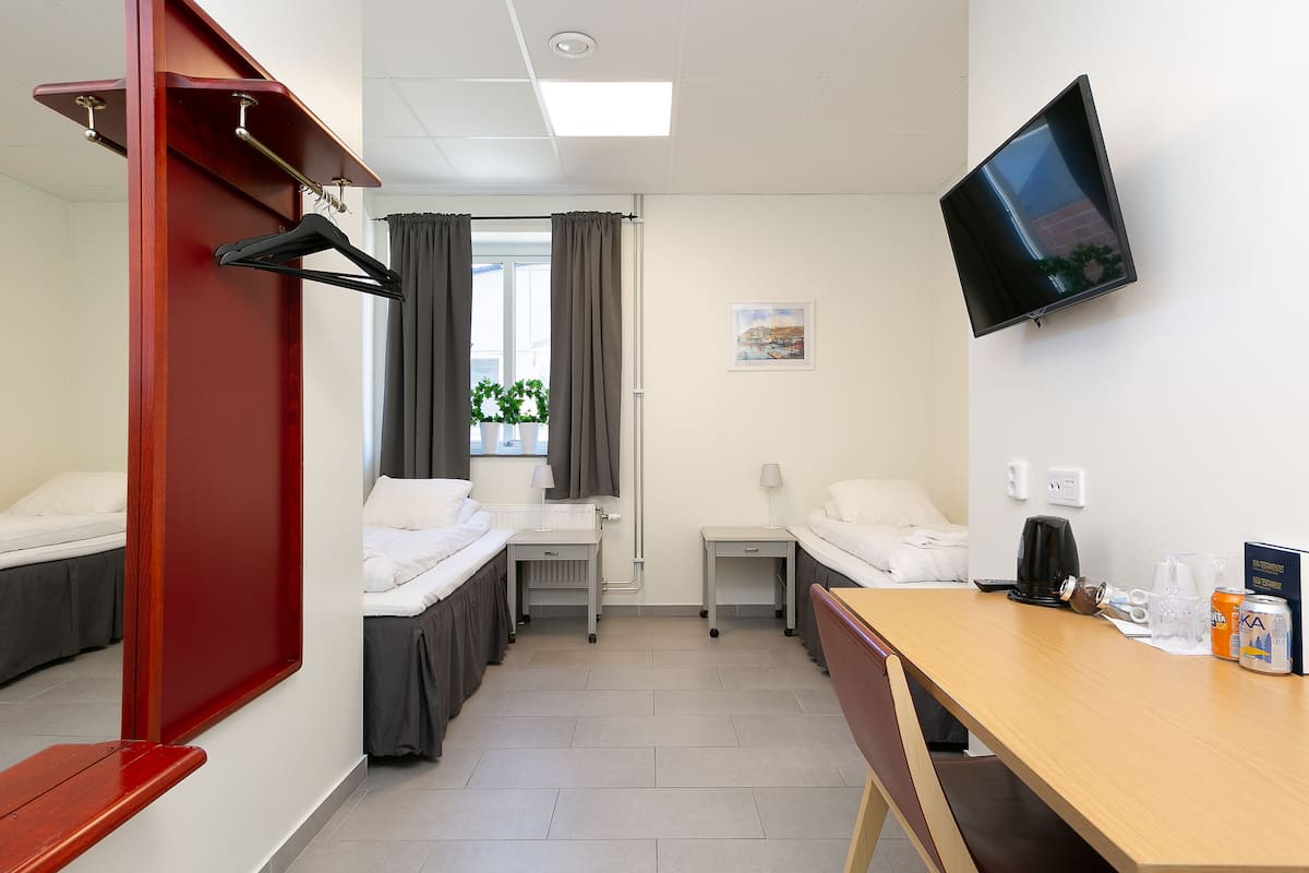 Habitación de hotel con dos camas, un escritorio, televisión y ventana con cortinas.