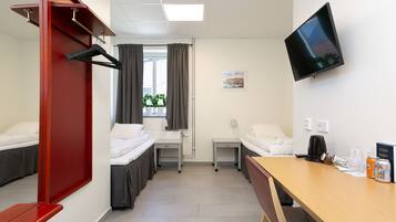 Ein Hotelzimmer mit zwei Betten, einem Schreibtisch, einem Fernseher und einem Fenster mit Vorhängen.