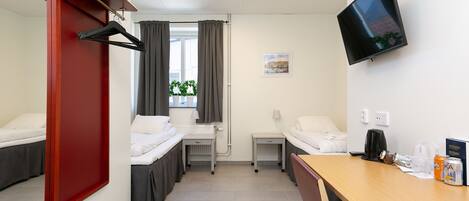 Habitación de hotel con dos camas, un escritorio, televisión y ventana con cortinas.