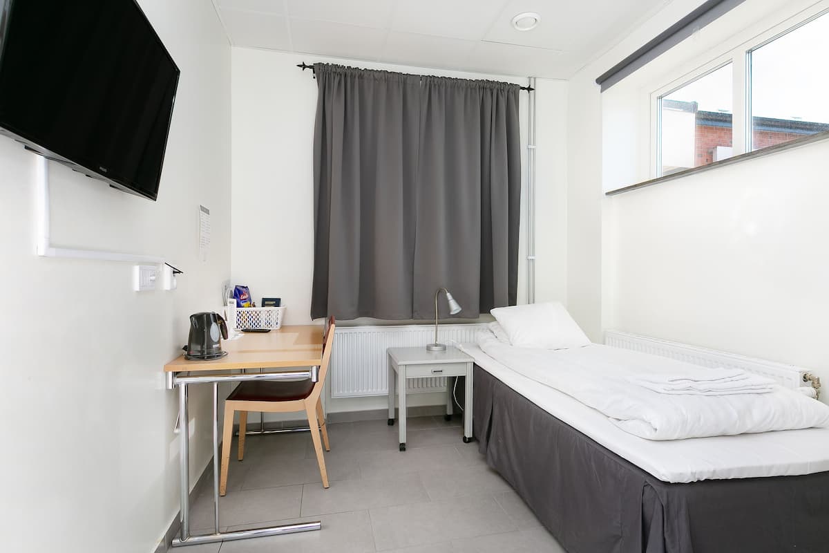 Habitación de hotel con cama, escritorio, silla, televisión y ventana con cortinas.