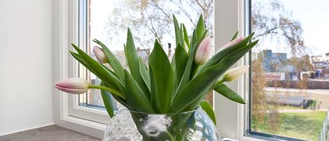 A clear glass vase with green leaves and pink tulips on a windowsill.