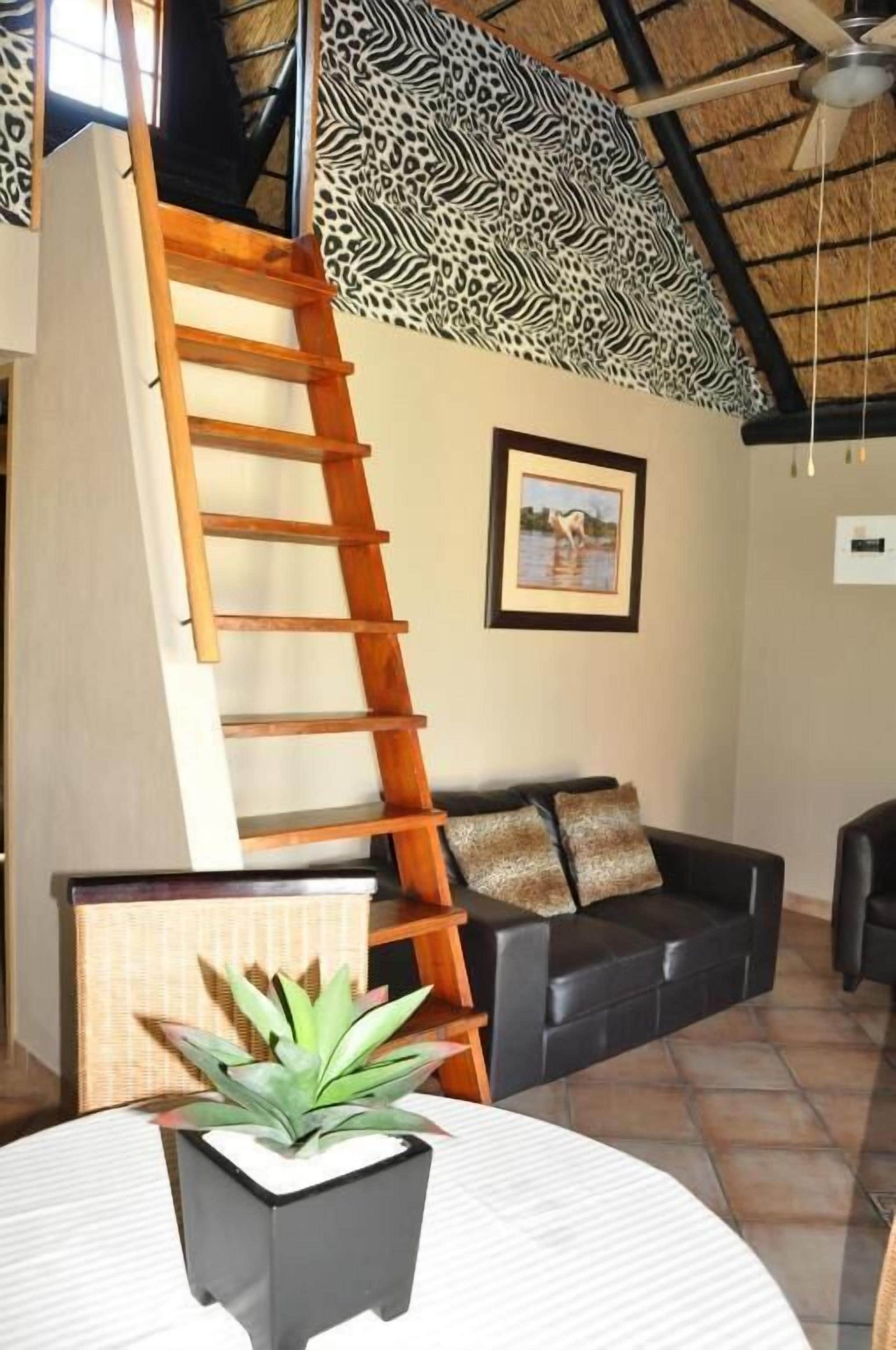 Una sala de estar con un sofá de cuero negro, una escalera de madera, un cuadro en la pared y una planta en maceta sobre una mesa redonda.