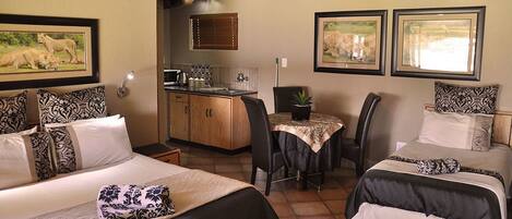 A hotel room with two beds, a kitchenette, a dining area, and artwork on the walls.