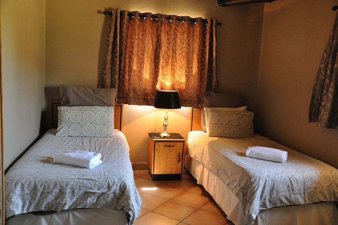 Una habitación con dos camas individuales, una mesita de noche con lámpara y una ventana con cortinas.