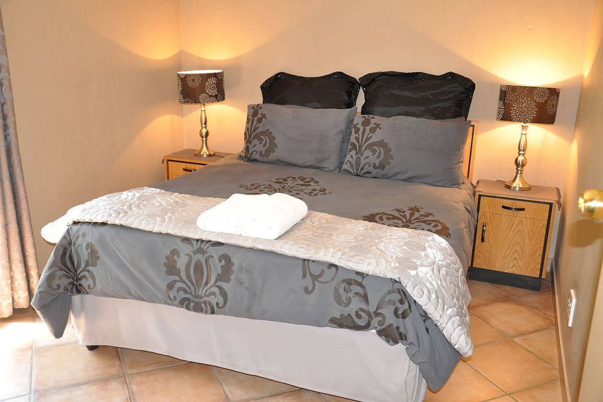 A neatly made bed with a white towel, two bedside tables with lamps, and a wooden nightstand with a drawer.