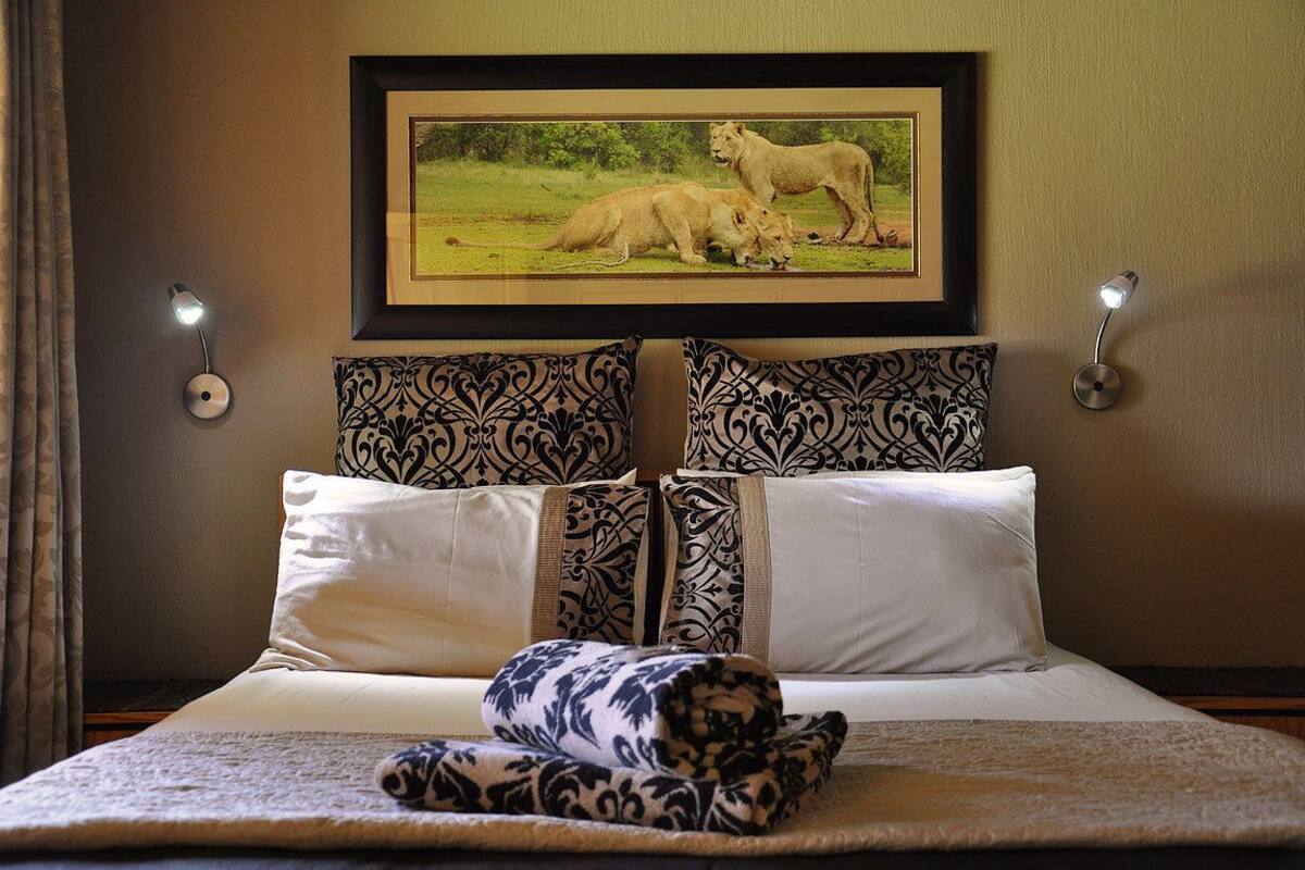 A bed with patterned pillows, a framed wildlife picture above it, and wall-mounted lights.