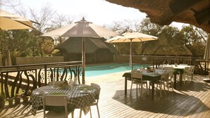Un espace extérieur avec une piscine, des tables et des chaises, des parasols et une structure dotée d’un toit de chaume.