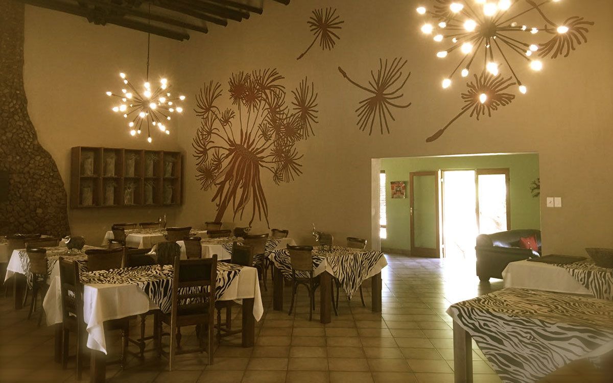 Comedor con mesas cubiertas de manteles estampados de cebra, sillas de madera y una pared decorada con arte abstracto.