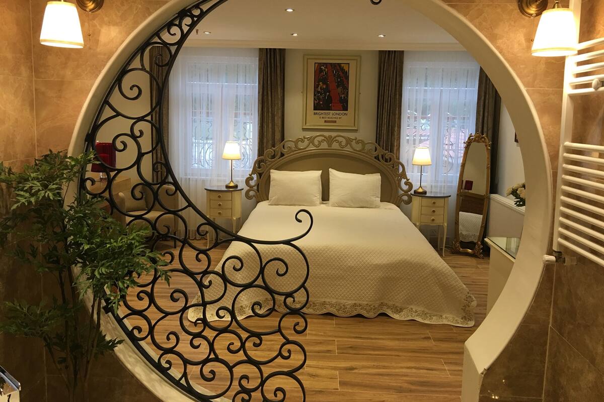Une chambre à coucher luxueuse, dotée d’un grand lit, d’une tête de lit richement décorée et d’un miroir rond encadrant la vue.