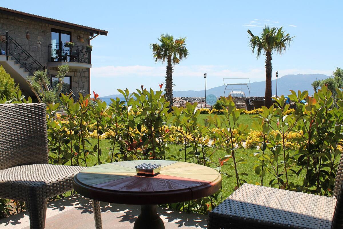 Une terrasse dotée de meubles en osier, d’une table ronde et offrant une vue sur les montagnes et la mer.
