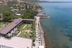 An aerial view of a coastal hotel with a long row of beachside rooms, a dining area with outdoor seating, and a clear view of the sea. - Assos Zeytinhan Hotel Special Class (Ayvacik)