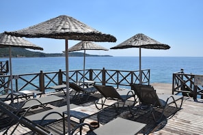 A deck with outdoor seating, including chairs and tables, overlooking a body of water. - Assos Zeytinhan Hotel Special Class (Ayvacik)