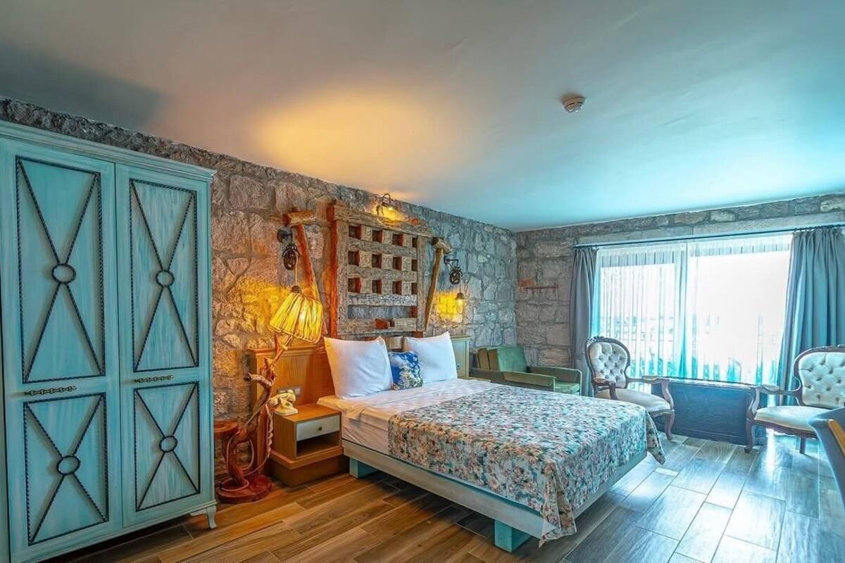 Une chambre à coucher avec un lit, des tables de chevet, une commode, un mur en pierre et une fenêtre avec des rideaux.
