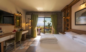 Habitación de hotel con cama, escritorio, silla, televisor y balcón con vistas.