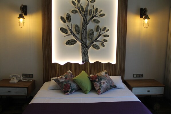A hotel room with a bed, floral pillows, a telephone on the nightstand, and wall-mounted lights. - Assos Zeytinhan Hotel Special Class (Ayvacik)