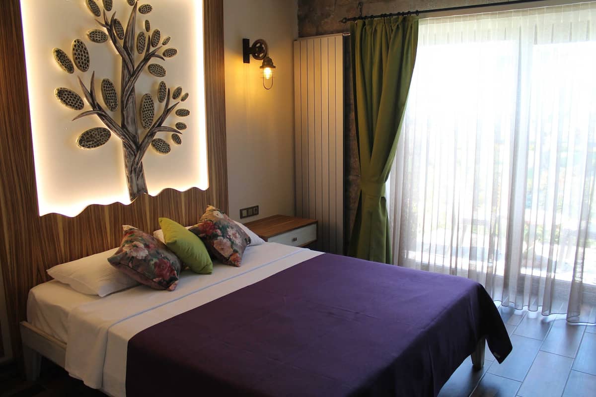A bedroom with a bed, pillows, a wall-mounted light fixture, a nightstand, and a window with curtains.