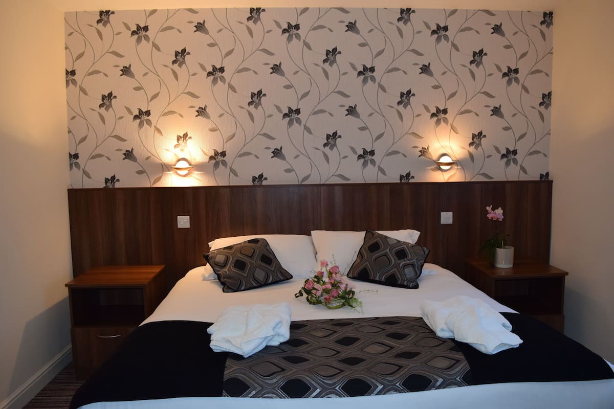 A hotel room with a bed, two nightstands, a floral wallpaper, and two wall-mounted lamps.