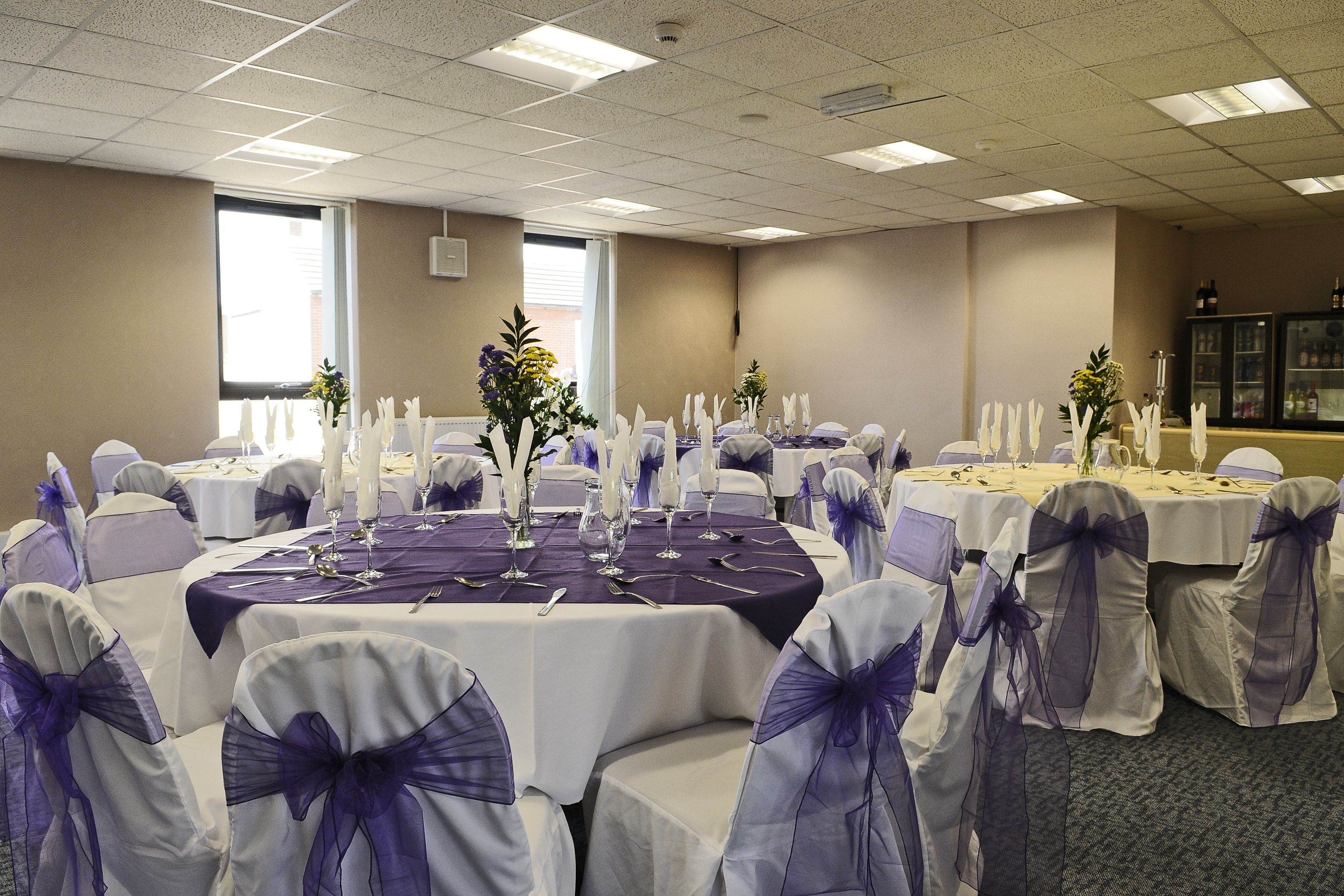 A banquet hall with round tables, white and purple tablecloths, and chairs with purple sashes.