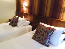 Habitación de hotel con dos camas, cada una con ropa blanca y almohadas decorativas.