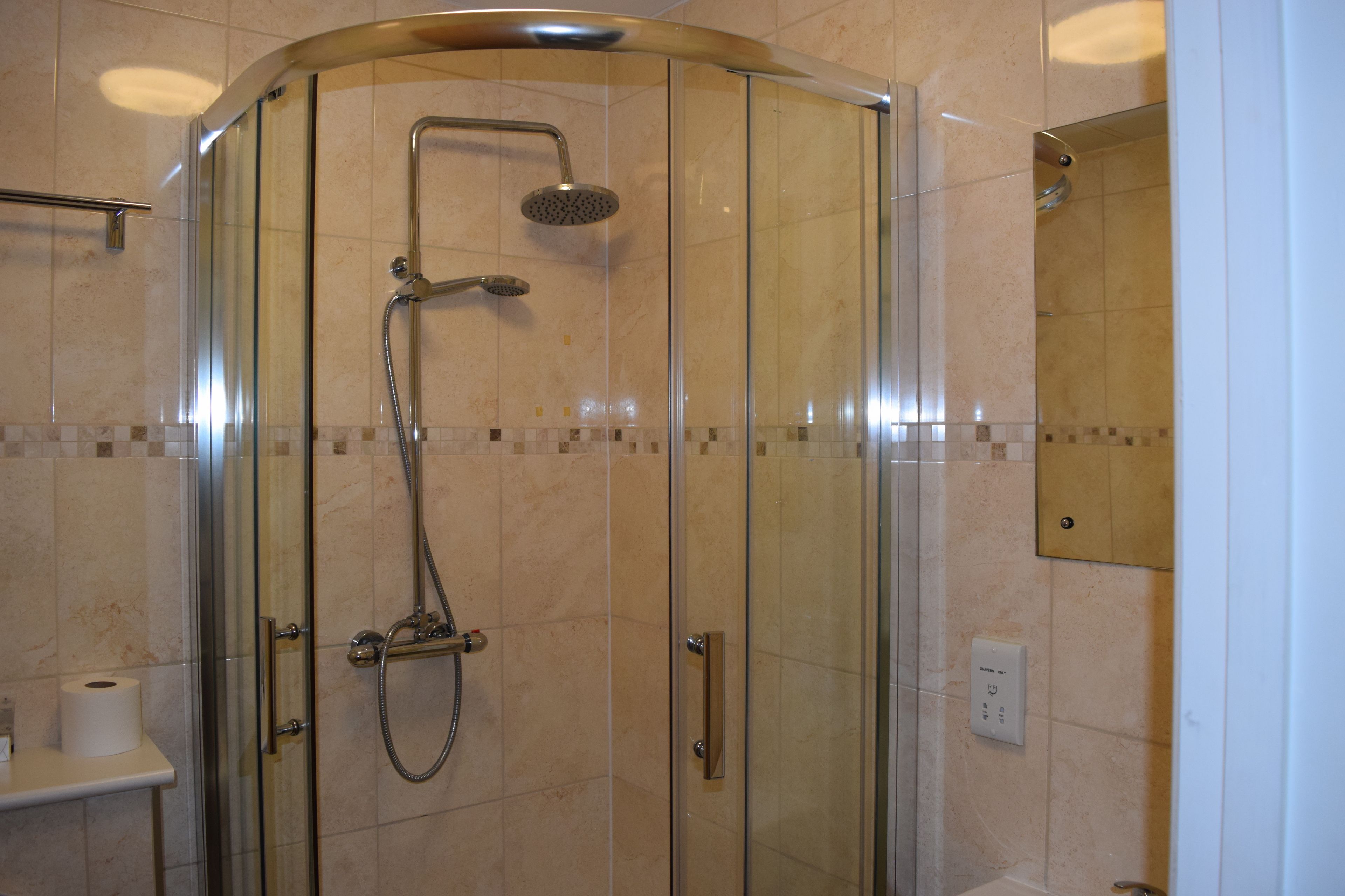 Ducha con cerramiento de vidrio, cabezal de ducha de mano y grifo empotrado.