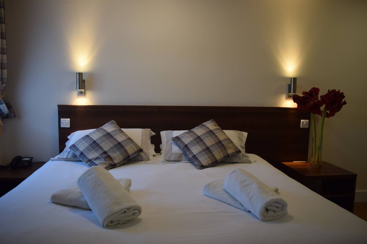 A neatly made bed with two rolled towels, a wooden headboard, and two wall-mounted light fixtures.