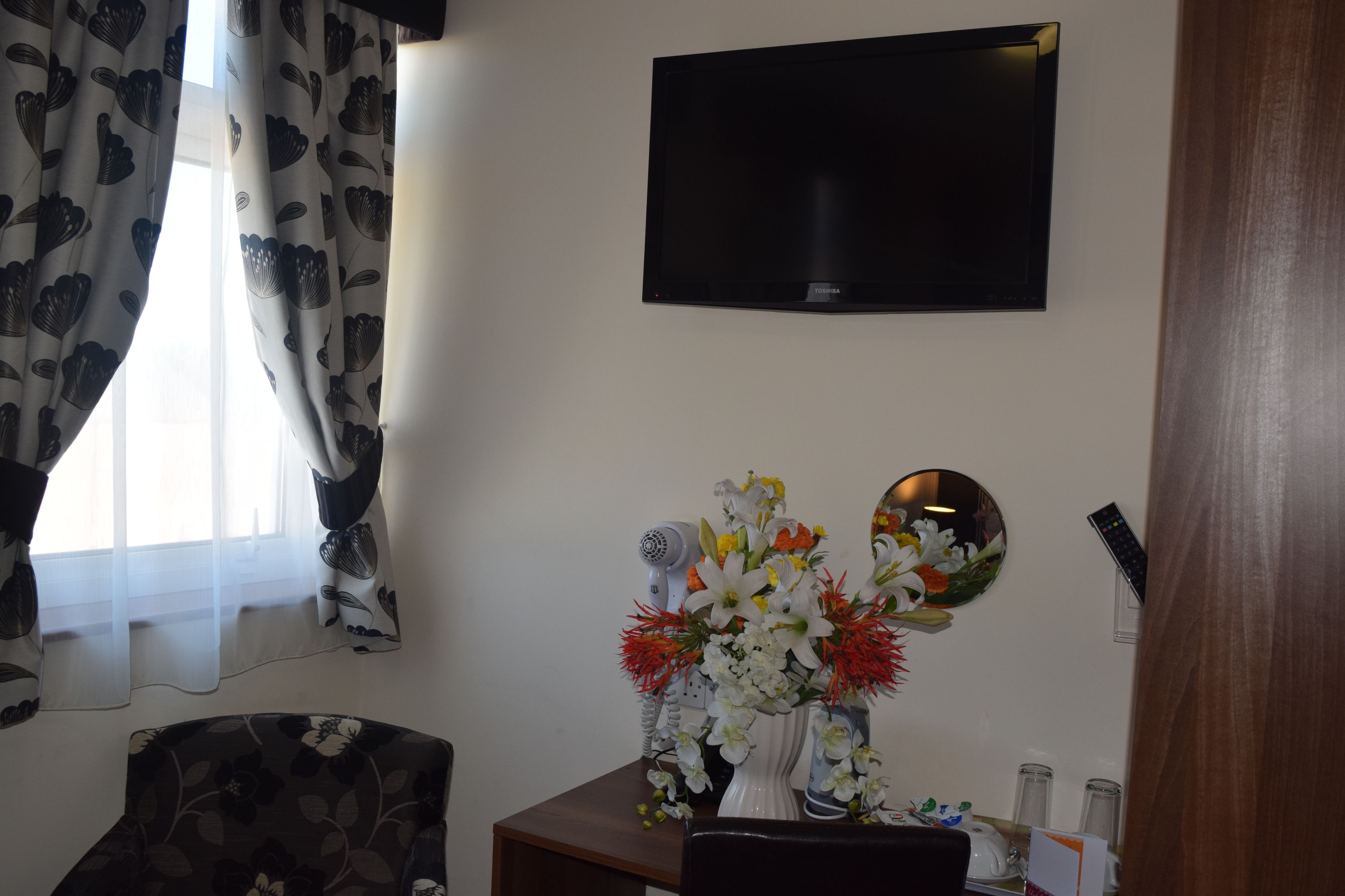 Una habitación con televisión de pantalla plana en la pared, un escritorio con un florero y una silla.