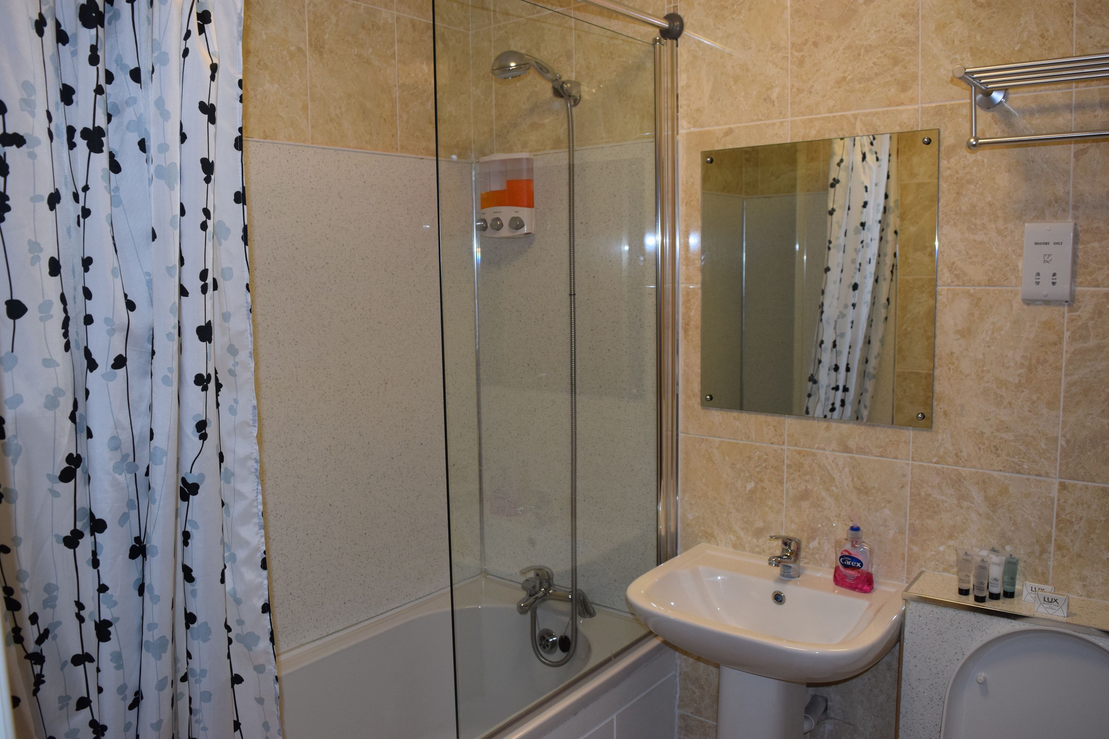 A bathroom with a glass-enclosed shower, a white sink, and a mirror above it.