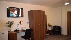 A hotel room with a wooden desk, a black chair, a wardrobe, a bed, a television, and a small refrigerator. - Star Anglia Hotel (Colchester)