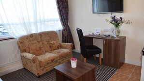 A furnished room with a sofa, a small table with a vase, a desk with a computer, and a TV on the wall. - Star Anglia Hotel (Colchester)