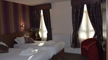 Una habitación de hotel con dos camas, una silla roja y un ventanal con cortinas.