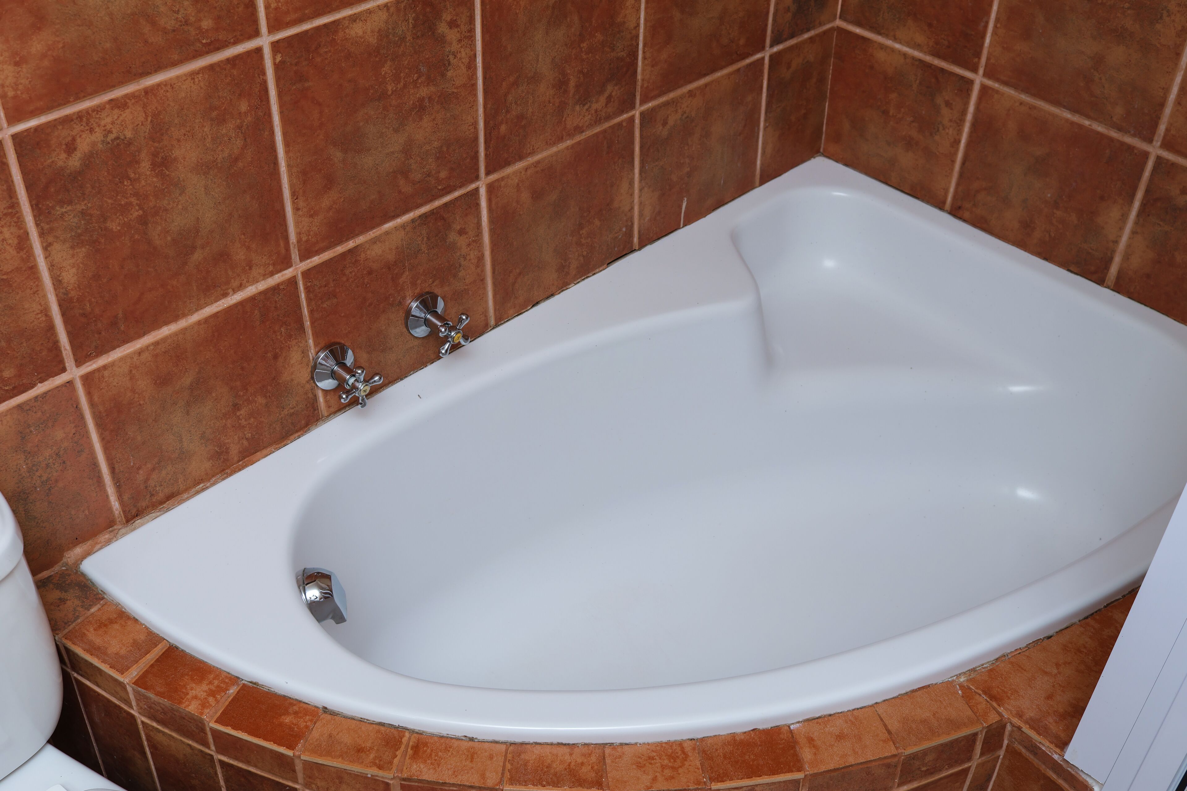 Una bañera blanca con accesorios de cromo en un baño con paredes de azulejos marrones.