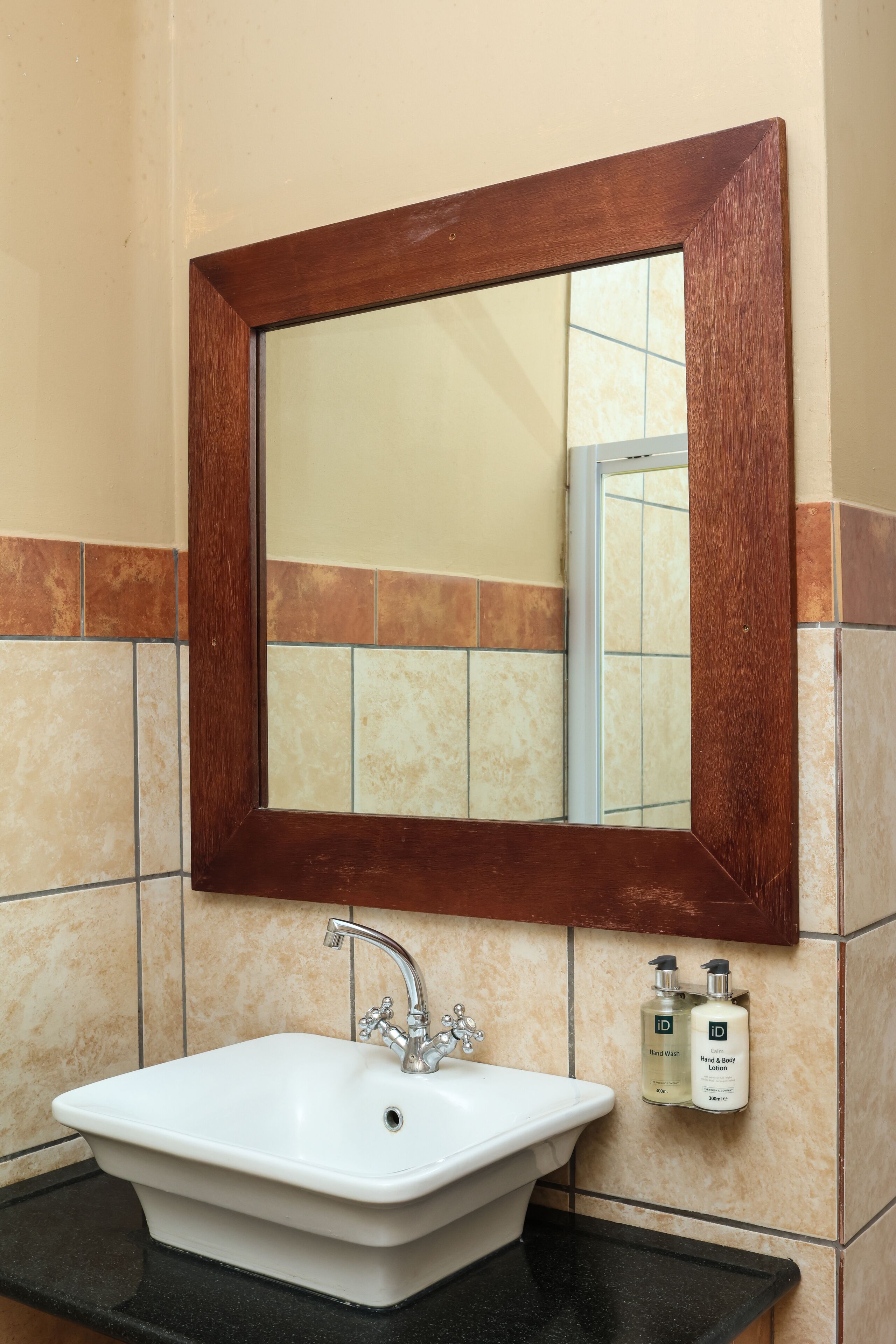 Un baño con lavamanos blanco, un espejo con marco de madera y dos botellas de jabón de manos en la pared.